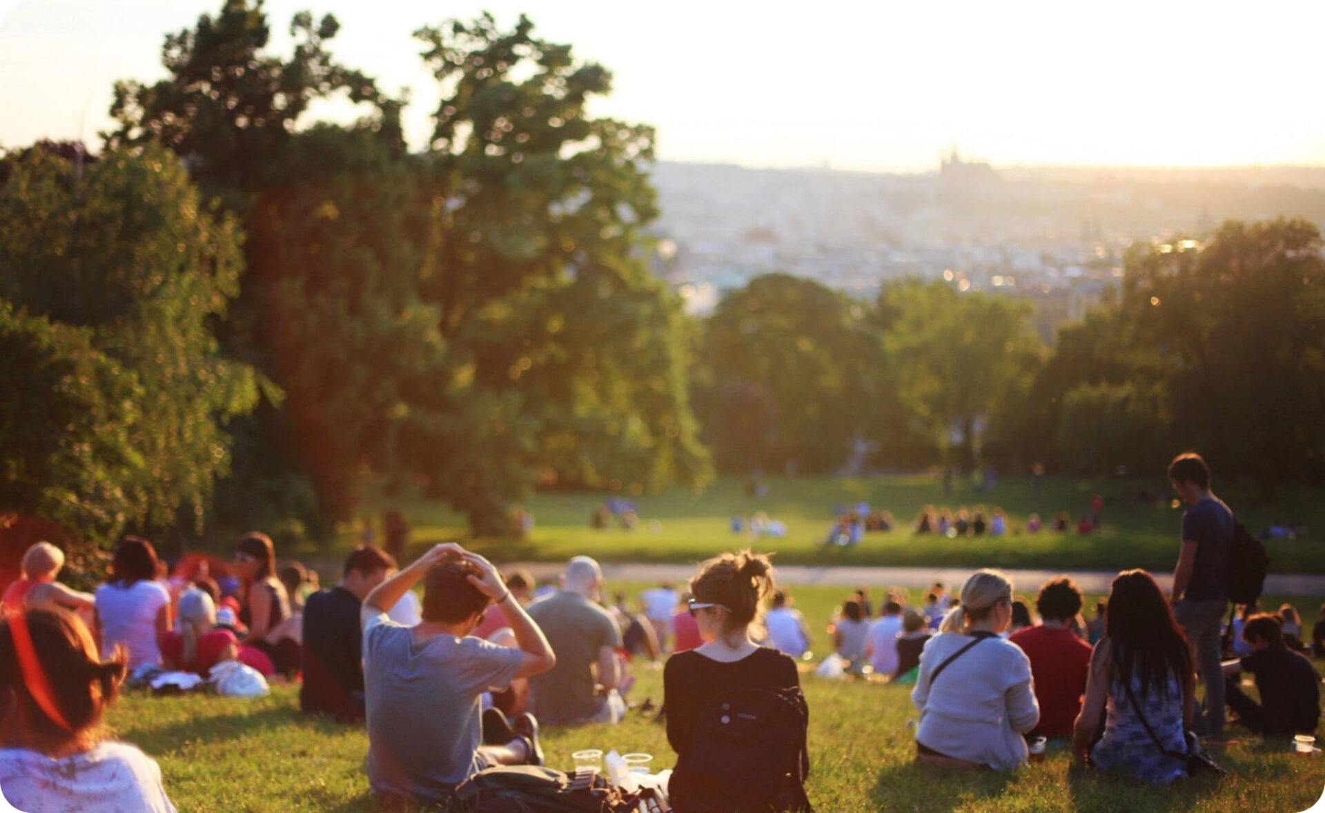 people sitting on the grass in a park as the sun sets