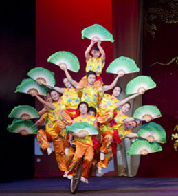 multiple acrobats riding a unicycle holding decorative fans